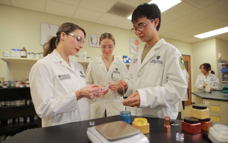 two UToledo pharmacy students assisted by a professor in lab
