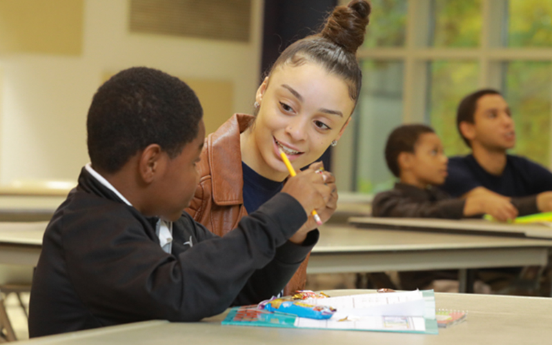 student teacher sits alongside elementary student in a classroom