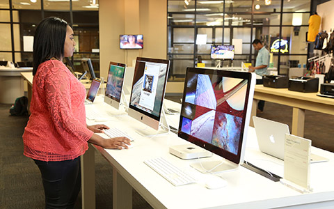 Woman stands in front of a row of mac computer monitors and observes one of the screens while holding the mouse
