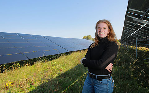 Woman in a field stands in front of a row of solar panels