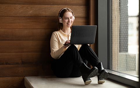 A woman sitting with a laptop and wearing headphones