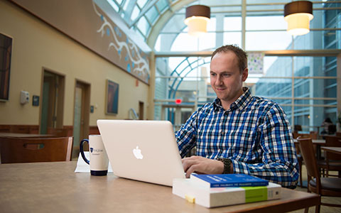 Man sitting at table with open laptop and textbook