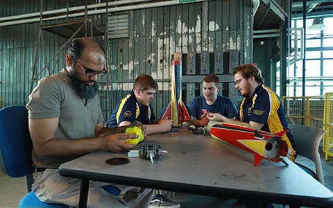 Engineering students sit at a table assembling a rocket
