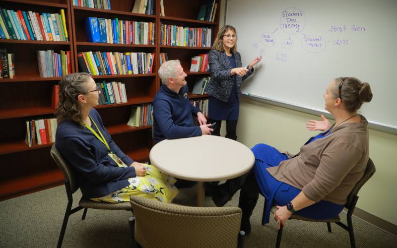 Group seated at a table in a conference room observe whiteboard presentation