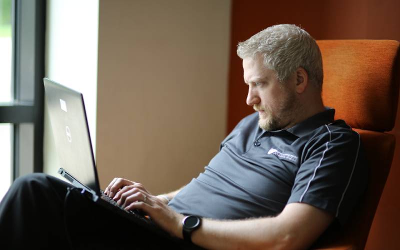 Online UToledo student seated in chair types on laptop keyboard