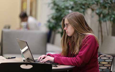 Student sitting at a table types on her laptop