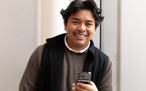 Male student smiling while holding a cell phone