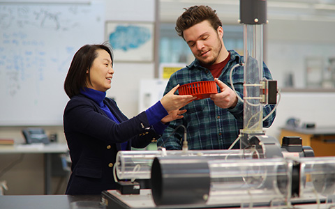Professor presents and hands over a red circular device to student at lab station