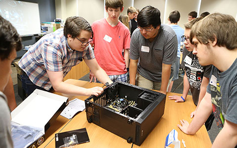 A group of students huddled around observing an unassembled computer